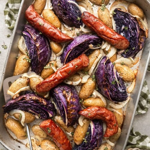 Overhead view of a sheet pan of Kielbasa and Potatoes with purple cabbage wedges.