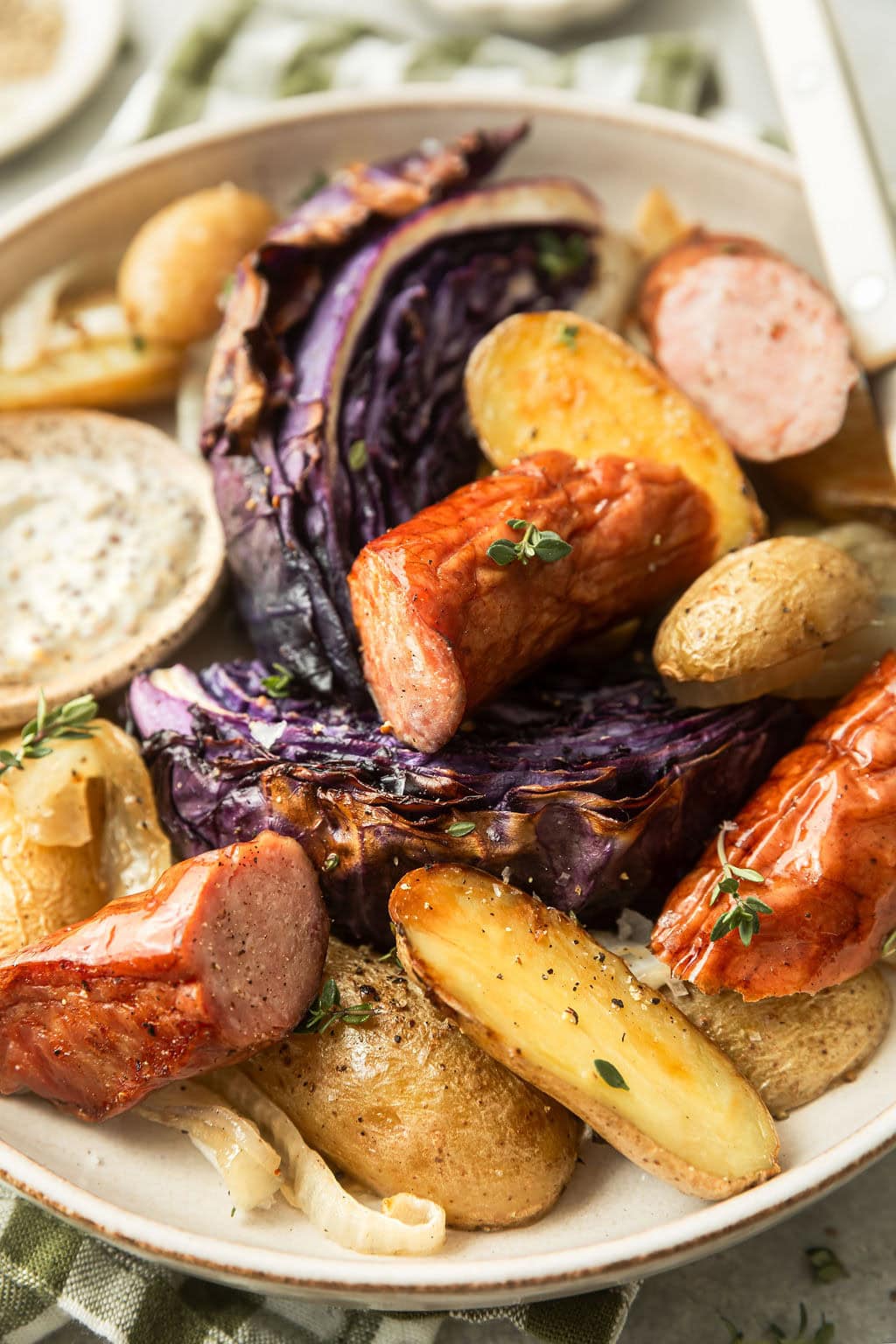 Close up view of a plate of Kielbasa and Potatoes with purple cabbage topped with fresh herbs.