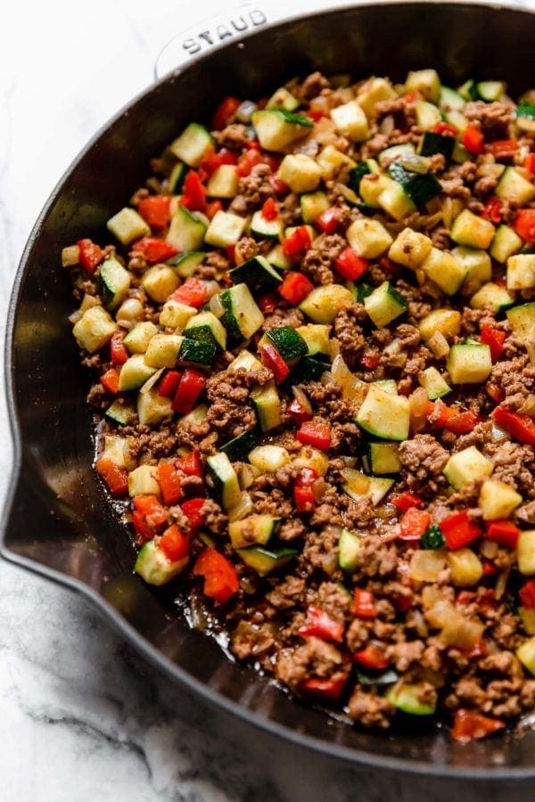 Taco meat with diced zucchini and red bell pepper in cast iron skillet