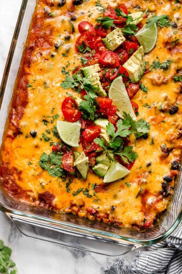 Overhead view healthy taco casserole in baking dish topped with melted cheddar cheese and diced tomatoes, avocado, and fresh cilantro.