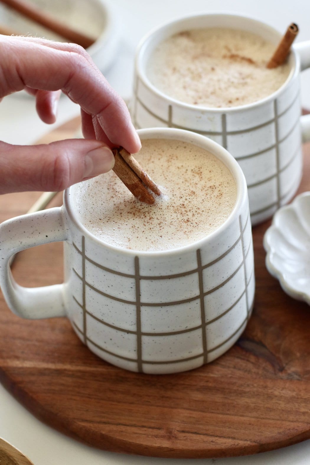 Close up view of a hand stirring a cinnamon stick into a freshly blended Cinnamon Coconut Latte. 