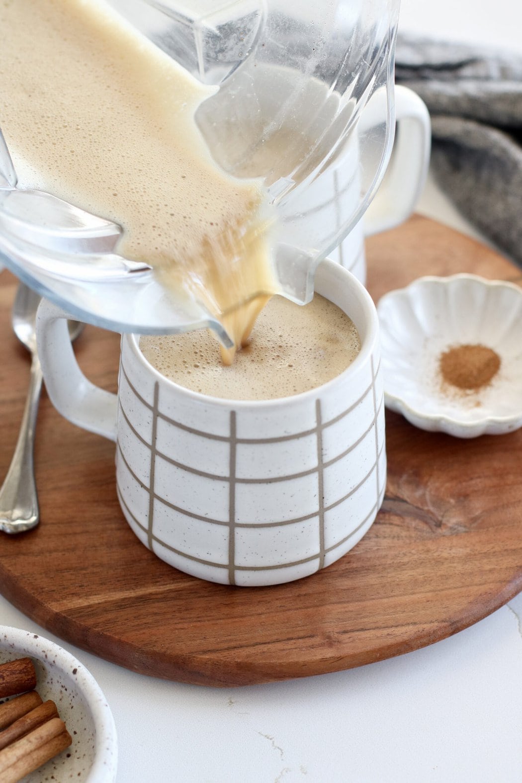 Close up view of a blender pouring freshly blended Cinnamon Coconut Latte into a white coffee cup. 