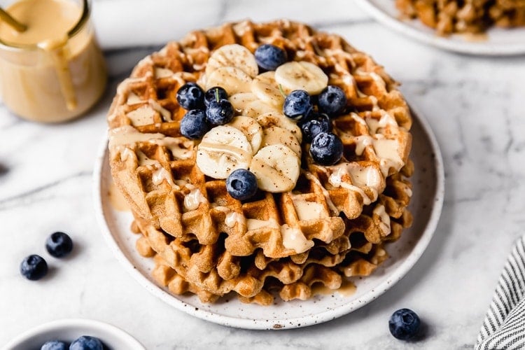 Close up view of a stack of peanut butter waffles topped with bananas and blueberries. 
