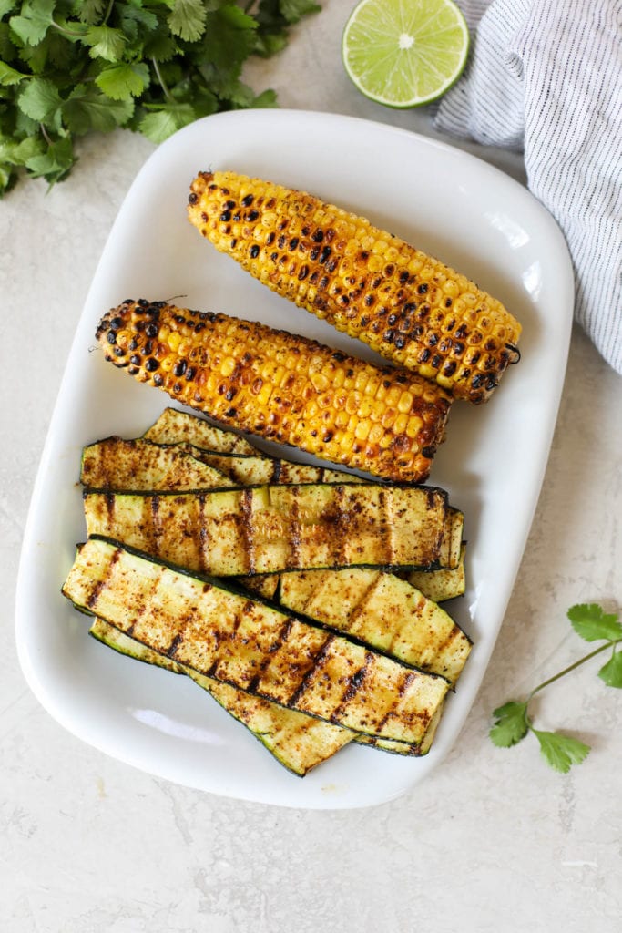 A rectangular white platter with grilled zucchini and corn - both are nicely grilled marked and slightly charred to make Grilled Salmon with Elote Style Veggies