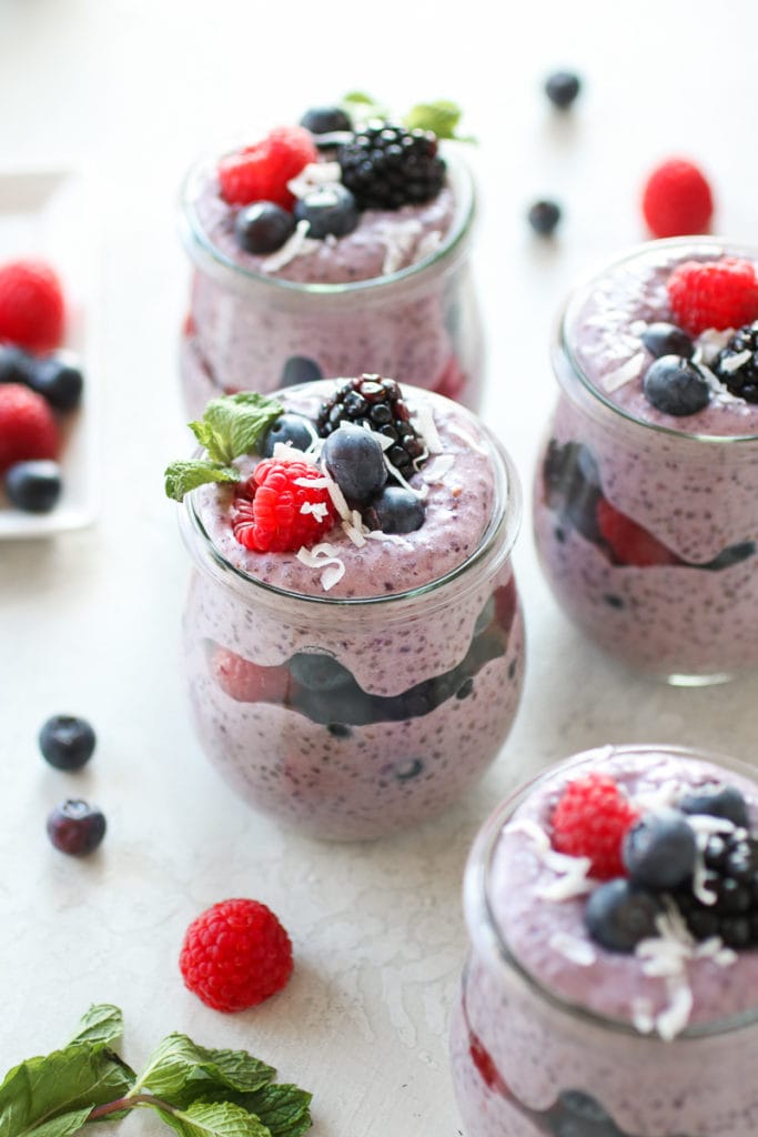 Photo of Mixed Berry Protein Chia Pudding in four glass jars layered with berries and garnished with a sprig of mint.