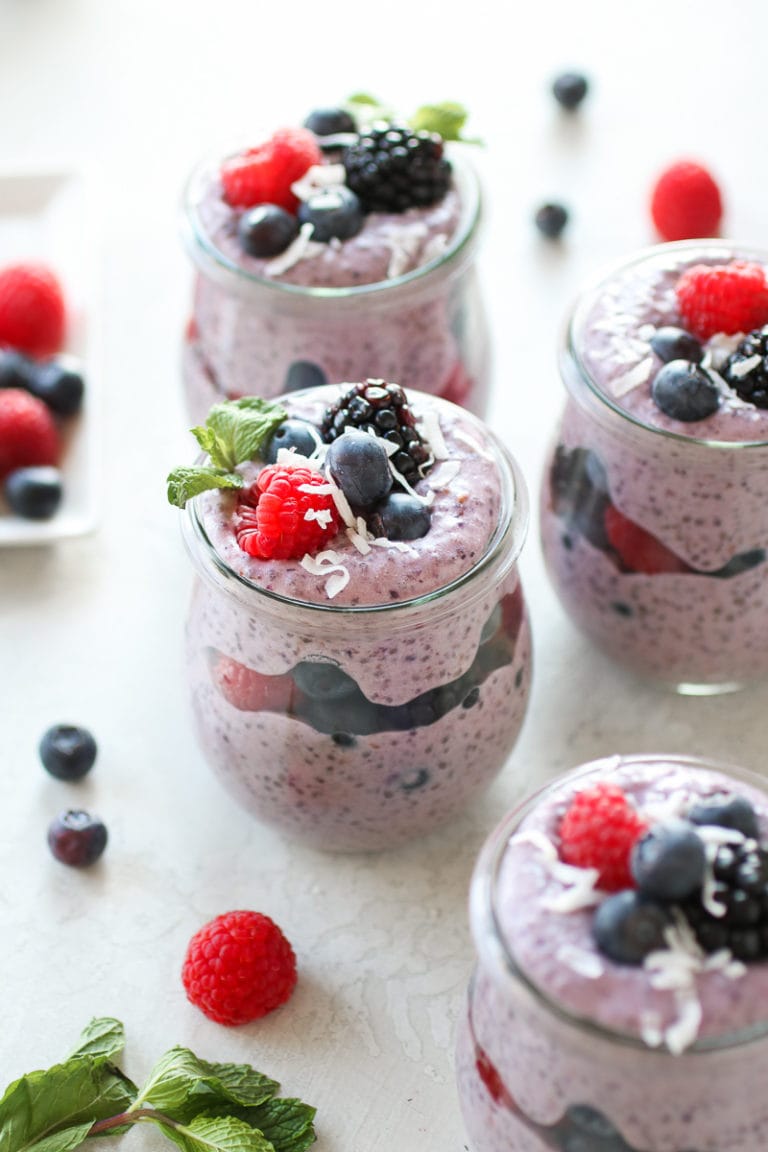 Parfait cups filled with layers of mixed berry protein chia pudding topped with fresh berries, coconut flakes, and mint leaves. 