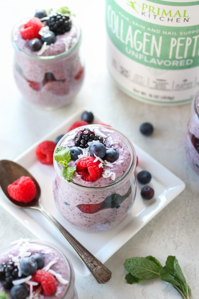 Photo of Mixed Berry Protein Chia Pudding in a jar on a square white plate, layered with berries and garnished with a sprig of mint. Canistered of Primal Kitchen Collagen Peptides in the background.