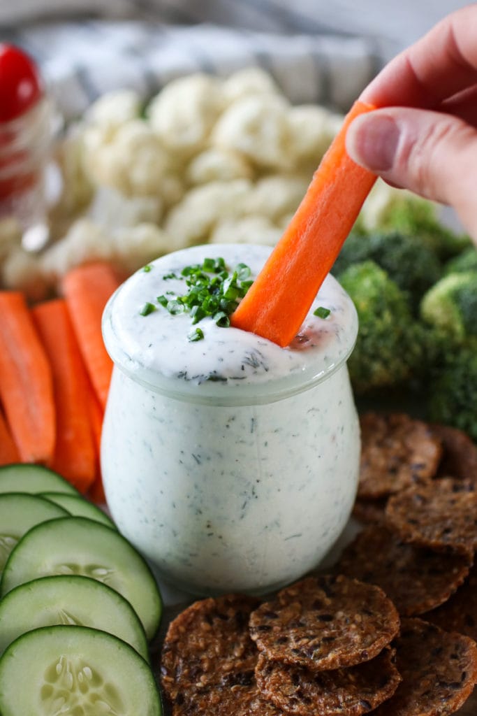 Photo of Healthy Homemade Ranch Dressing in a mason jar topped with fresh chives and surrounded by fresh cut vegetables.