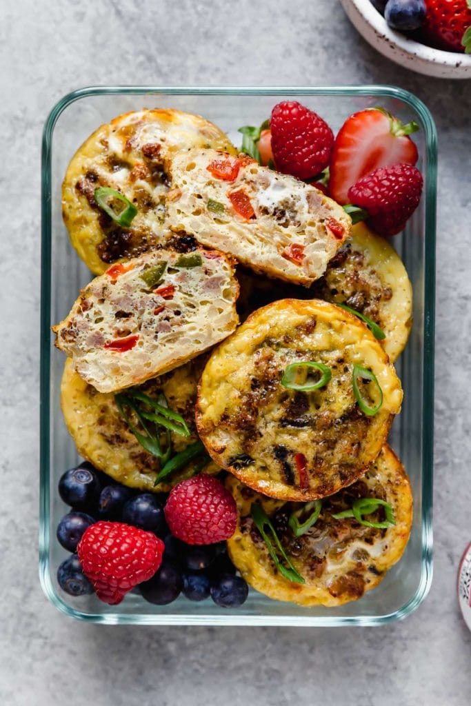 Overhead view of breakfast egg bites and fresh fruit in a glass meal prep container. 