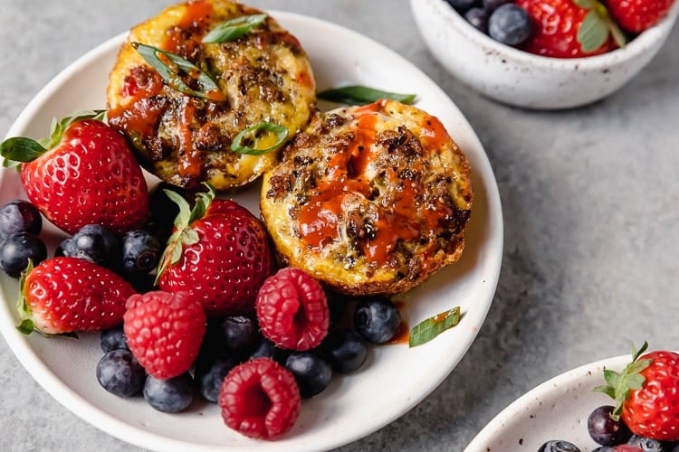 Two sausage hash brown egg muffins on plate with side of fresh berries.