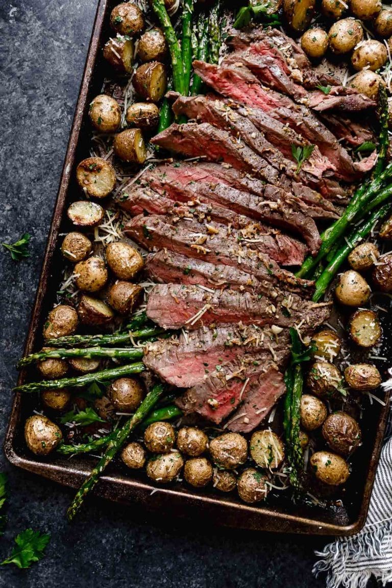 Sheet pan filled with parmesan crusted steak, cut into strips, baby potatoes and roasted asparagus