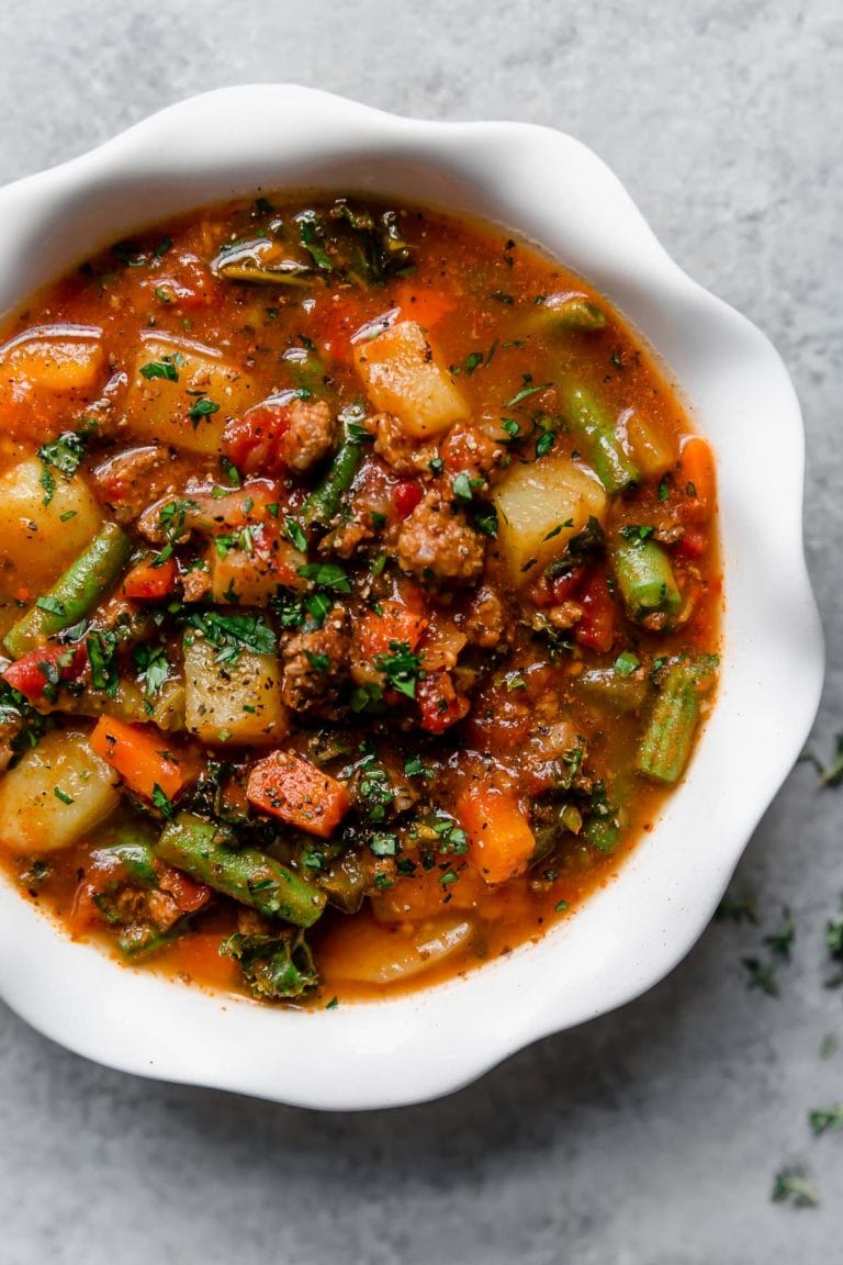 Overhead view of a bowl of hamburger soup topped with fresh herbs and black pepper. 