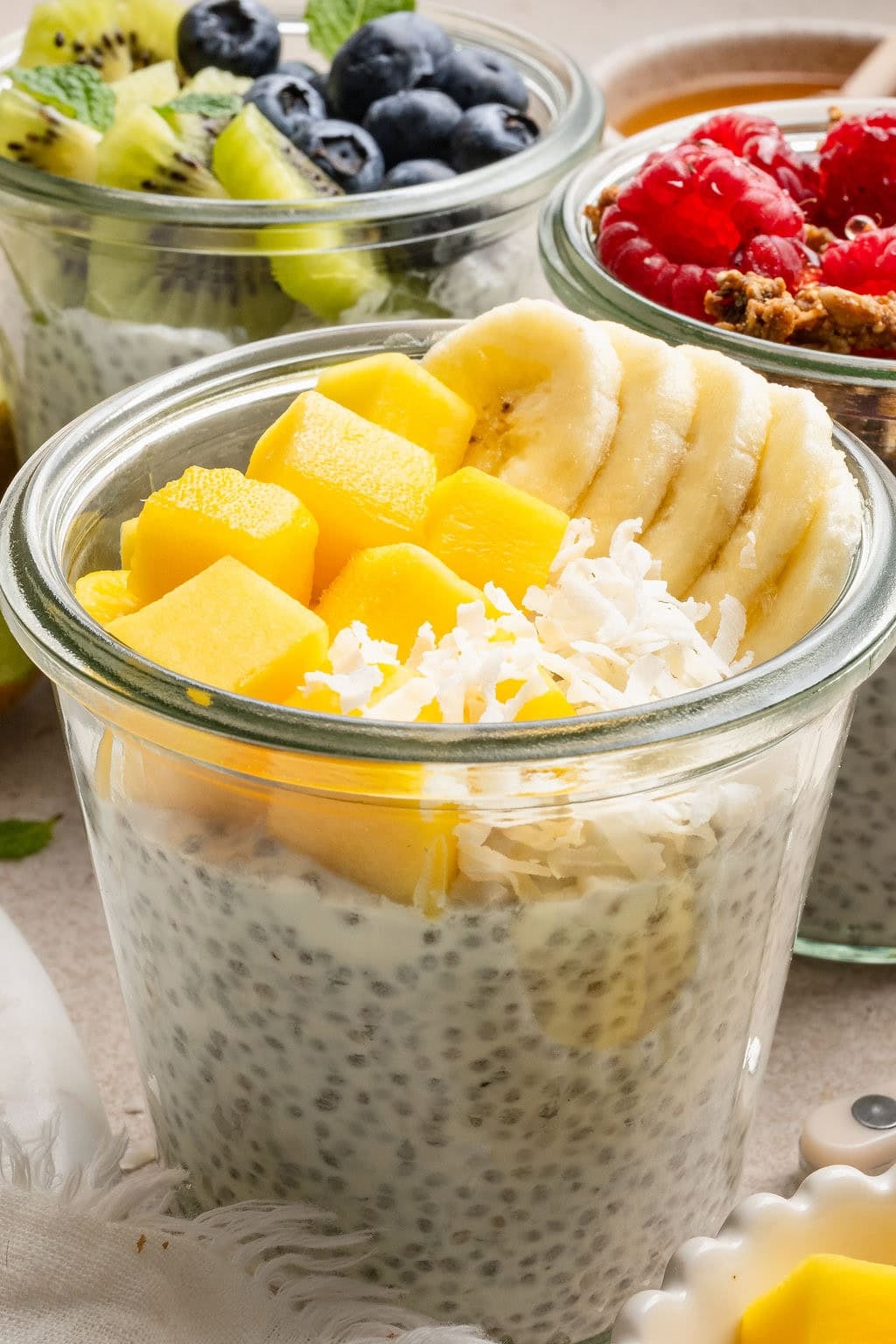Close up view of a glass jar of chia pudding topped with sliced mangos, bananas, and sprinkled with coconut flakes.