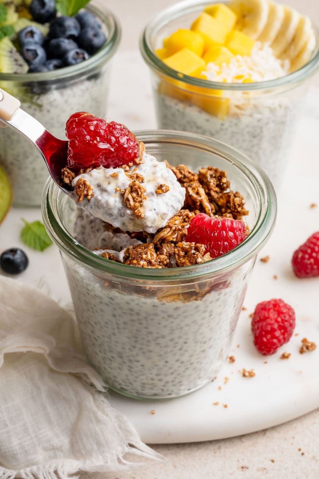 Close up view of a glass jar of chia pudding topped with raspberries and granola