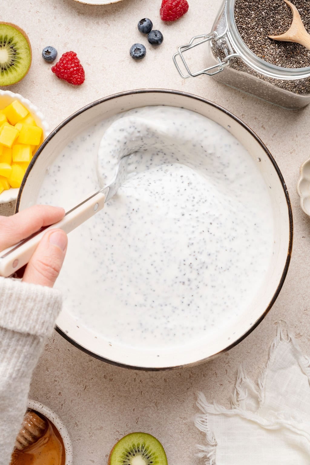Overhead view of a hand stirring chia pudding ingredients in a large white bowl.