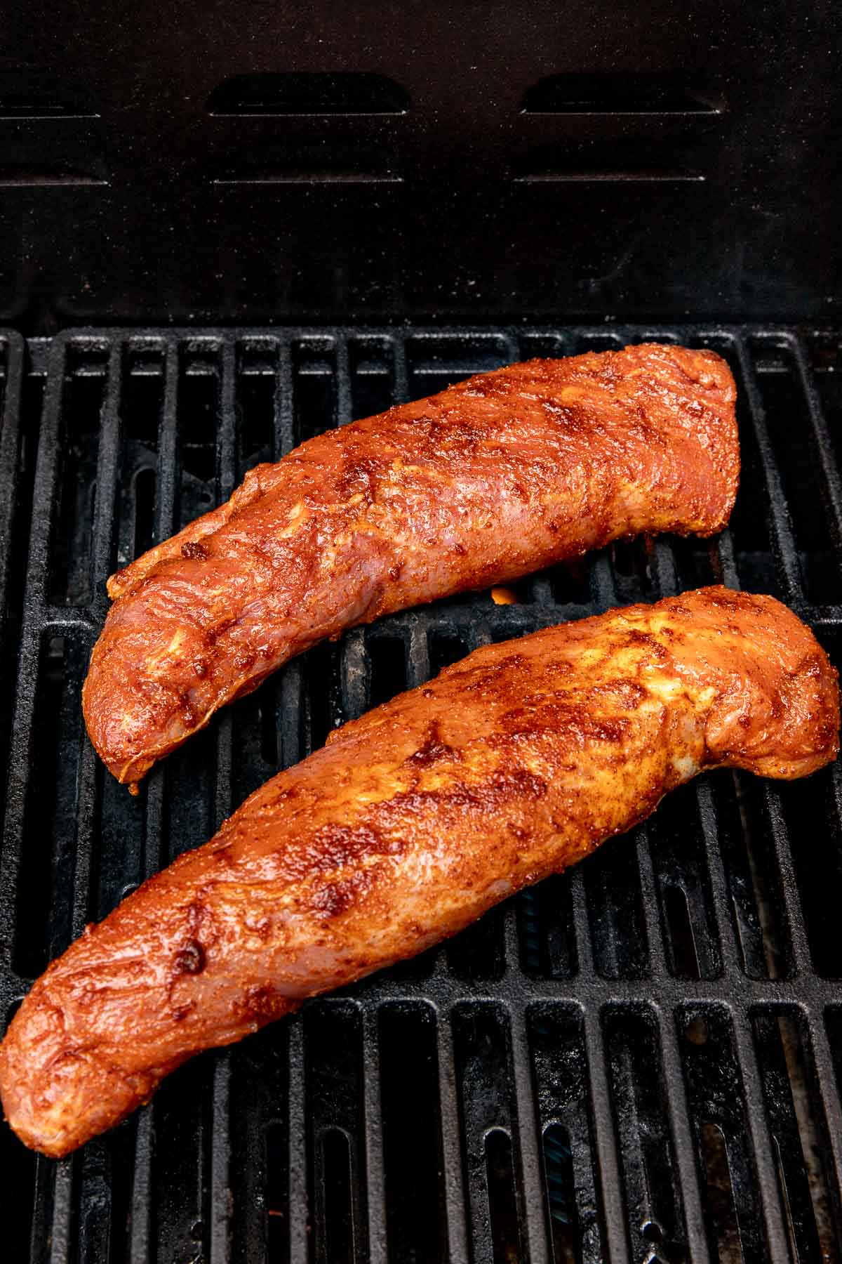 Two pork tenderloins on a grill after being coated with a wet spice rub mixture.