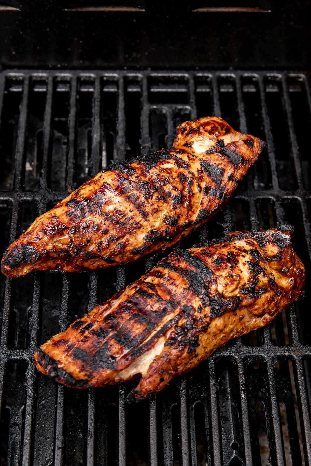Angled view of two grilled pork tenderloins on a grill.