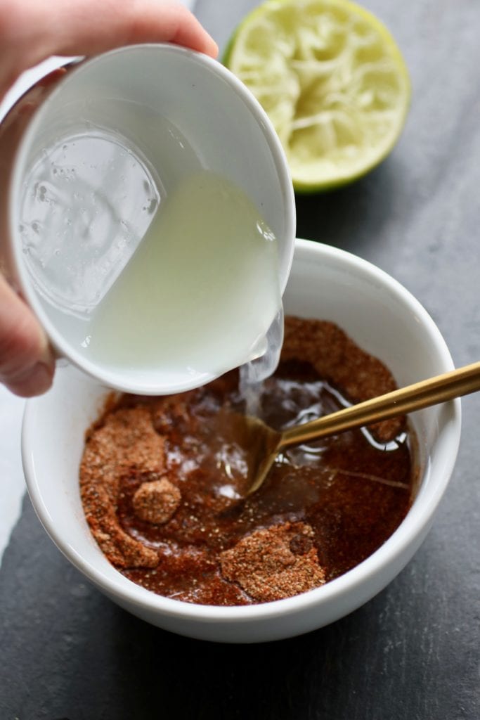 Photo of lime juice being poured into a white bowl on a black board holding the spice mix for the Ultimate BBQ Rub.