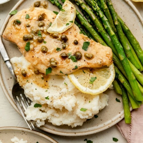 Overhead view of lemon chicken piccata on a plate with mashed potatoes and steamed asparagus.
