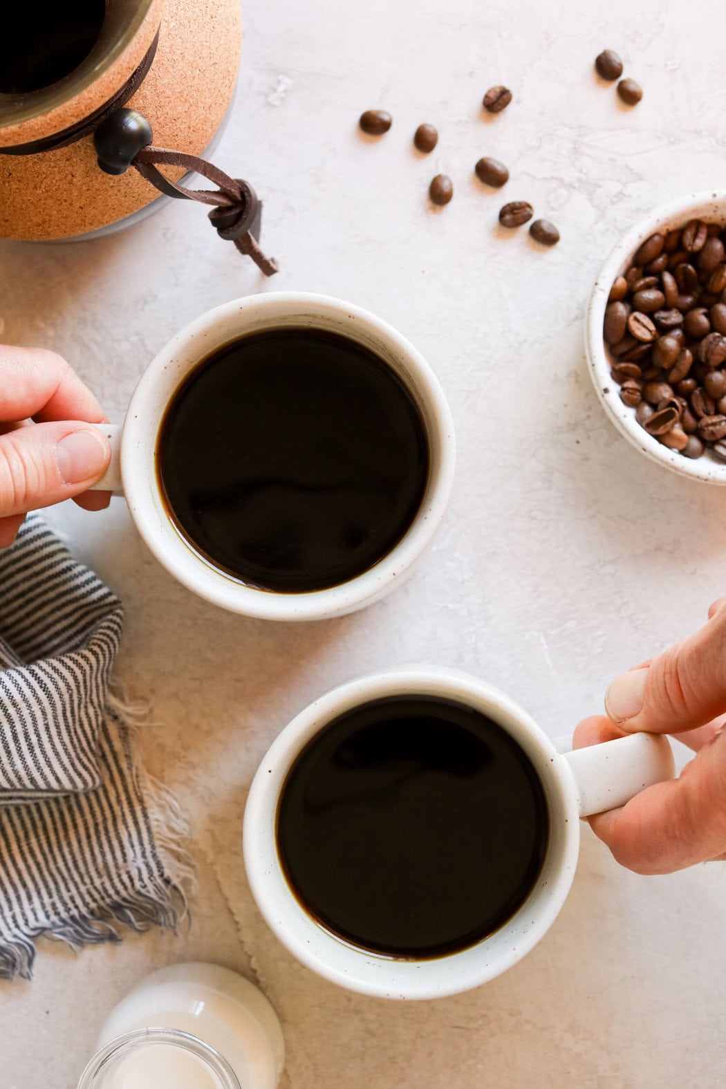 Overhead view of a hand holding a coffee cup and a bowl of coffee beans next to it. 