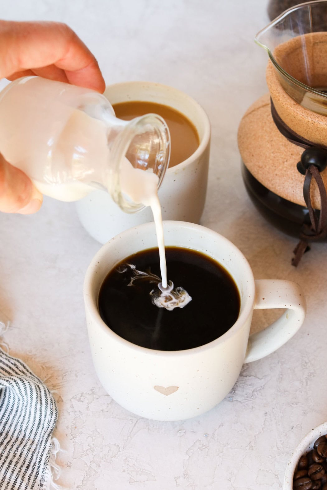 A close-up view of a hand pouring fresh cream into a cup of black coffee. 