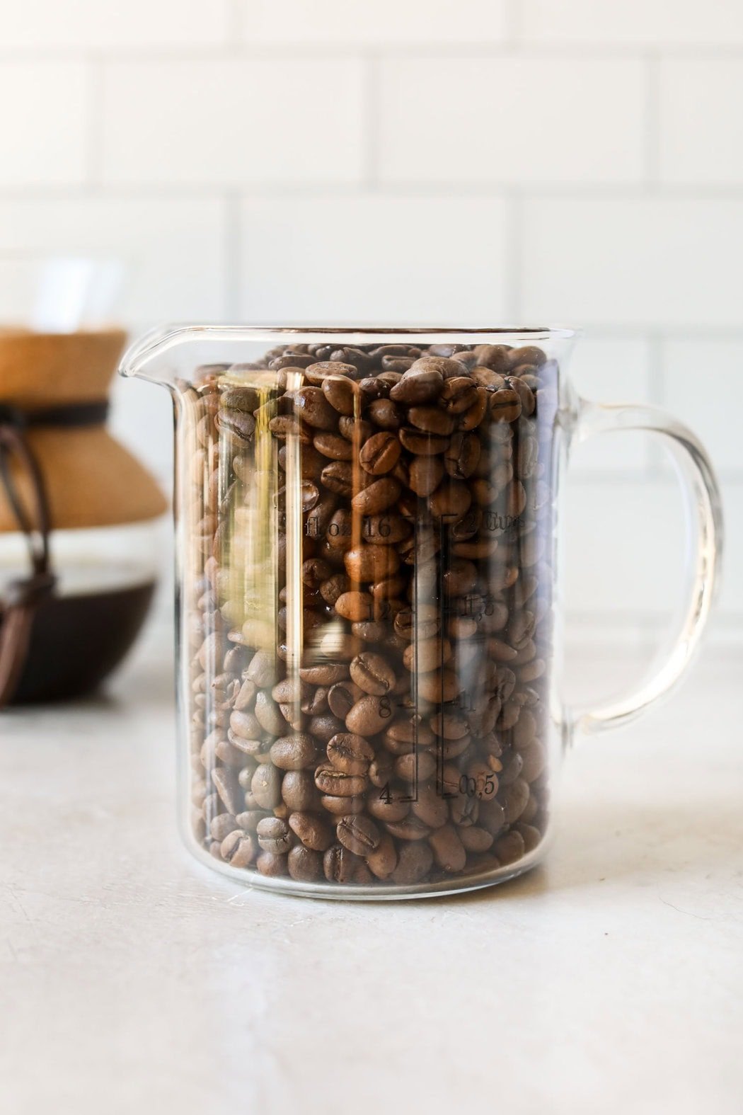 Close up view of a measuring cup filled with whole coffee beans. 