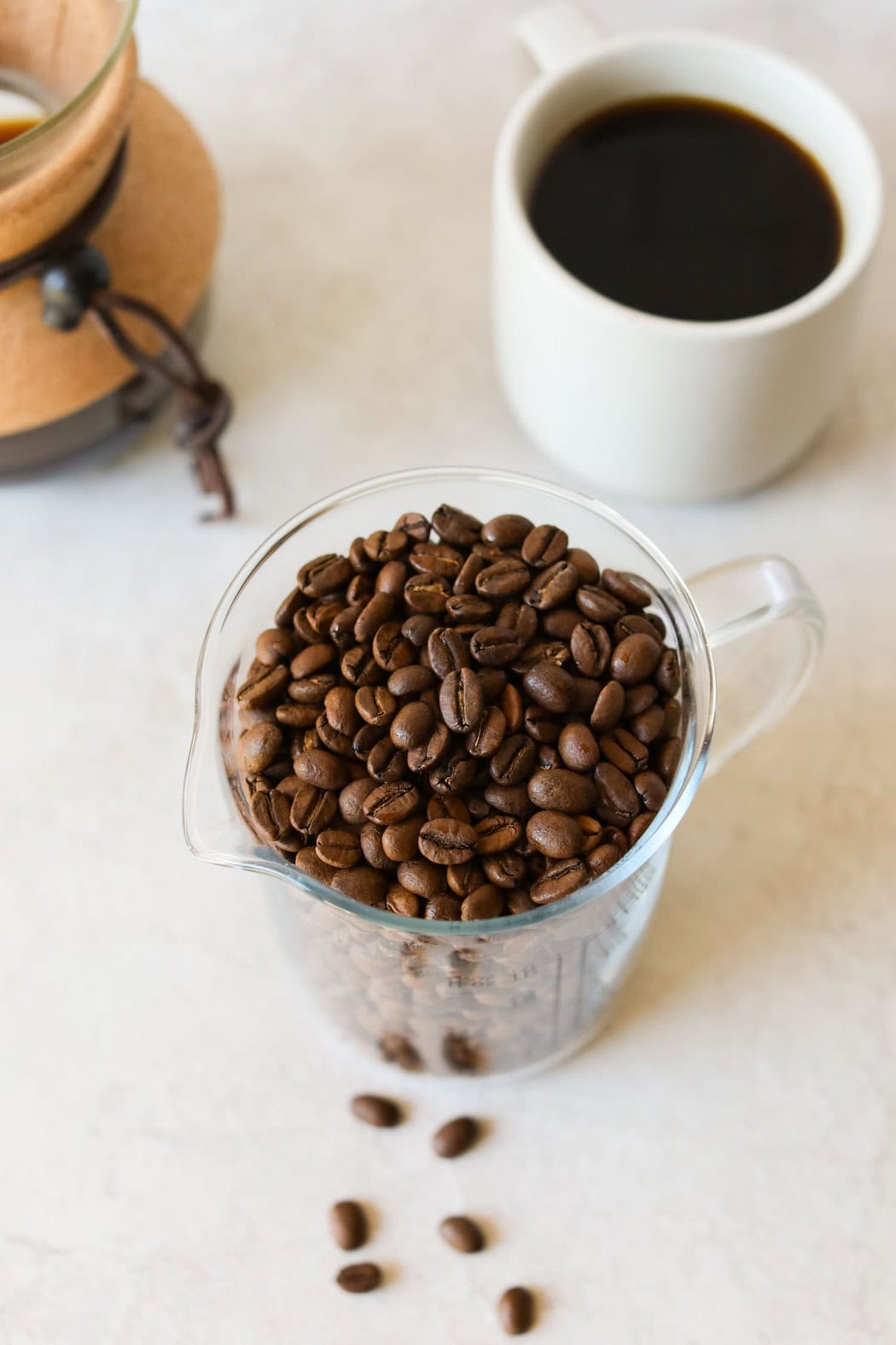 Close up view of a cup of whole coffee beans next to a cup of coffee. 