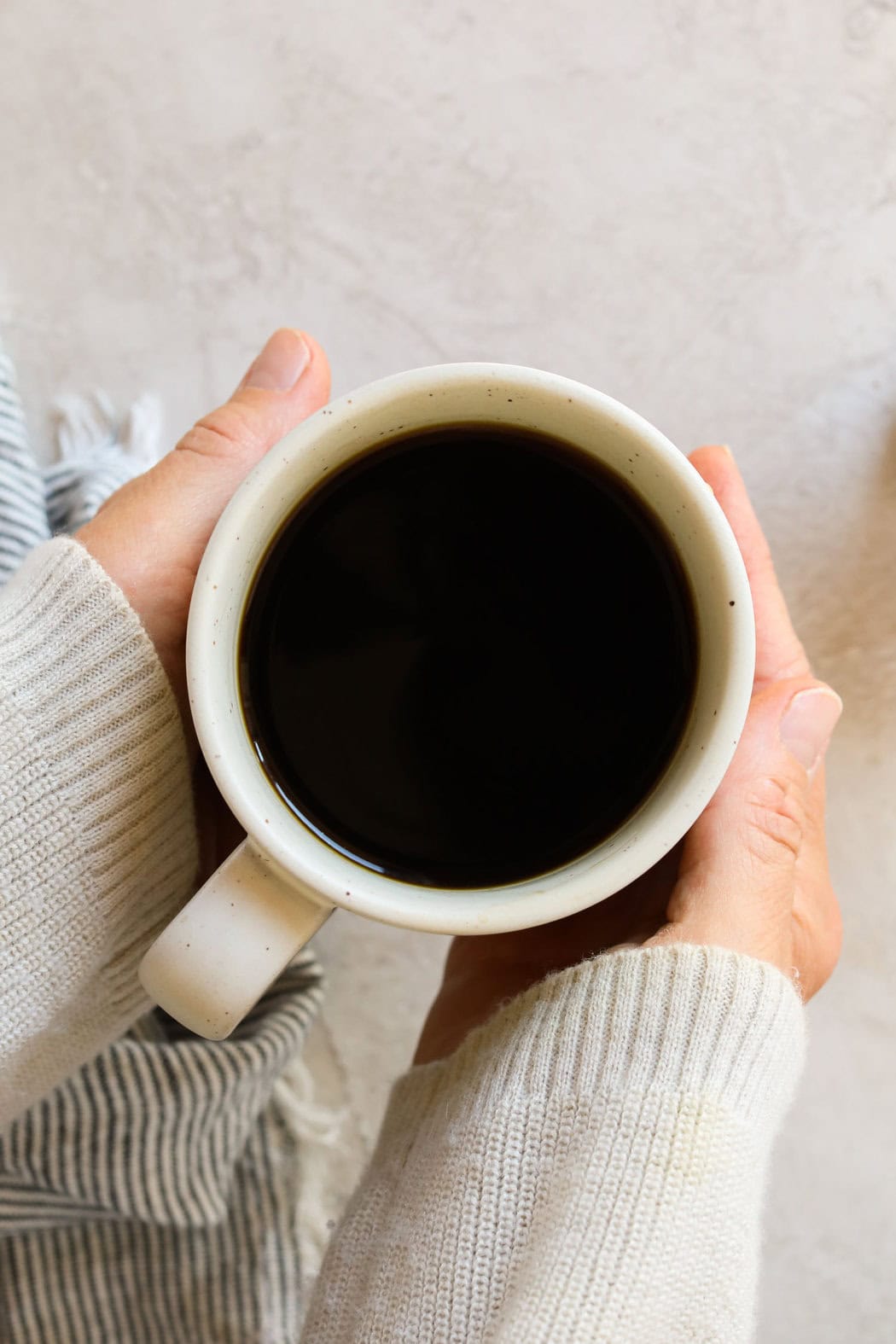 Two hands holding a cup of coffee in a white mug. 