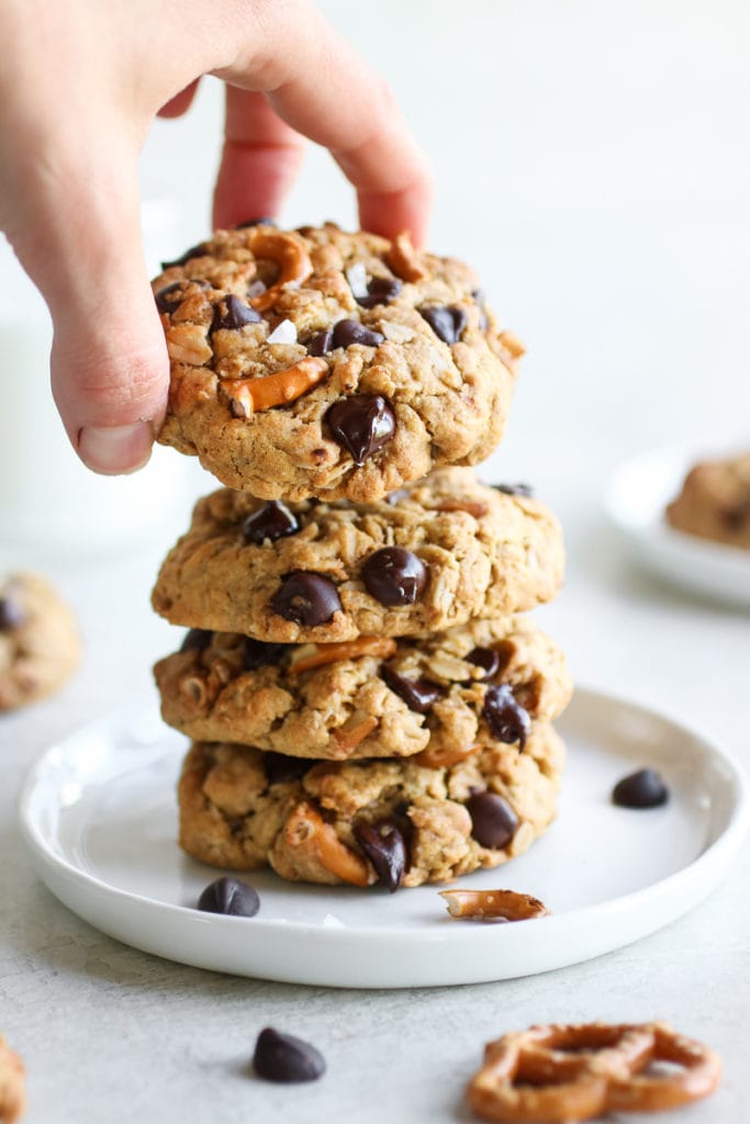 A stack of 4 peanut butter chocolate chip pretzel cookies showing a hand grabbing the top cookie. 