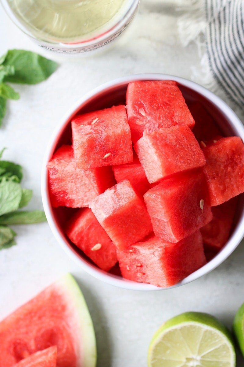 Photo of a bowl of cubed watermelon with sliced limes beside it. 