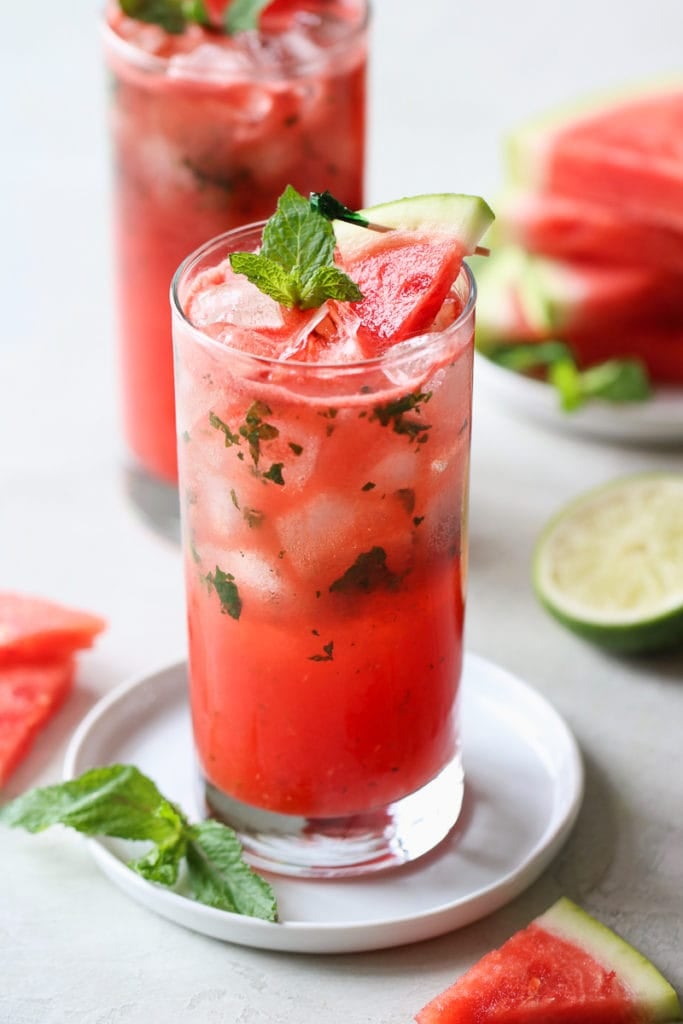 Side view tall glass filled with watermelon mojito garnished with mint and watermelon slice.