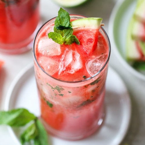 Overhead view watermelon mojito in tall glass garnished with mint sprig and watermelon slice.