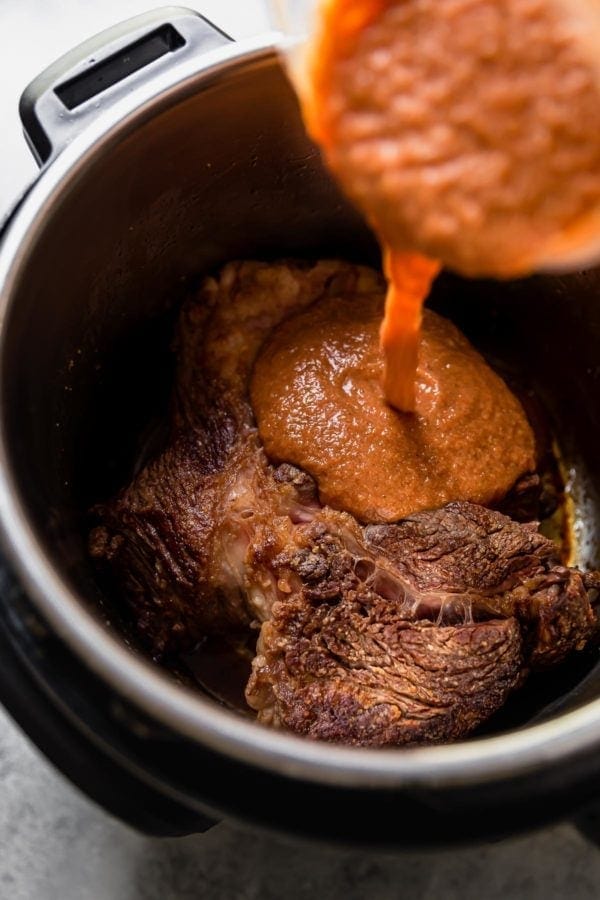 Sauce pours from a blender container onto a seared beef chuck roast in an Instant Pot.