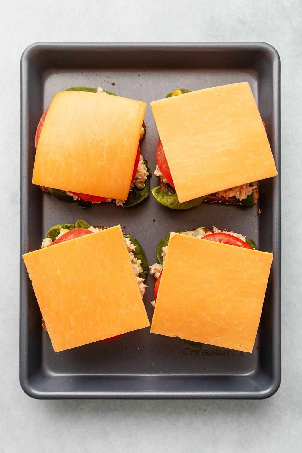 Overhead view of opened faced tuna melts topped with sliced cheese ready for the oven.
