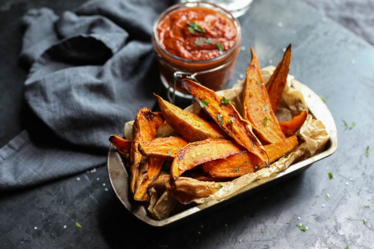 Roasted sweet potato wedges in parchment lined pan with bbq sauce on side.