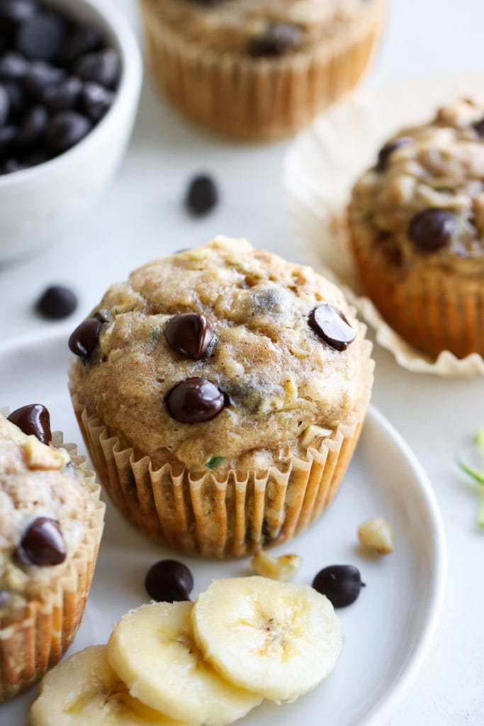 Close up side view Chocolate Chip Zucchini Muffin on white plate with banana slices on side.