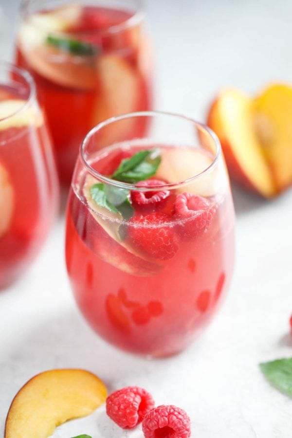Three stemless wine glasses filled with Raspberry-Peach Rosé Sangria are ready to be shared with friends.