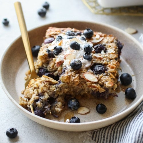 Serving of blueberry baked oatmeal in shallow bowl, topped with yogurt and fresh blueberries