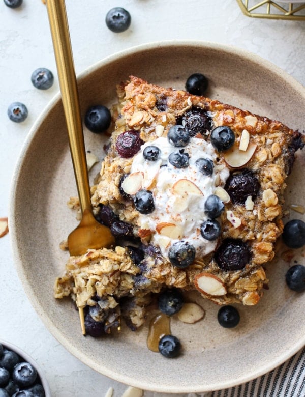Serving of healthy blueberry baked oatmeal in stone shallow bowl, topped with yogurt and fresh blueberries.
