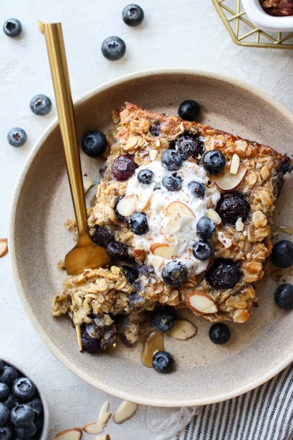 Serving of healthy blueberry baked oatmeal in stone shallow bowl, topped with yogurt and fresh blueberries.