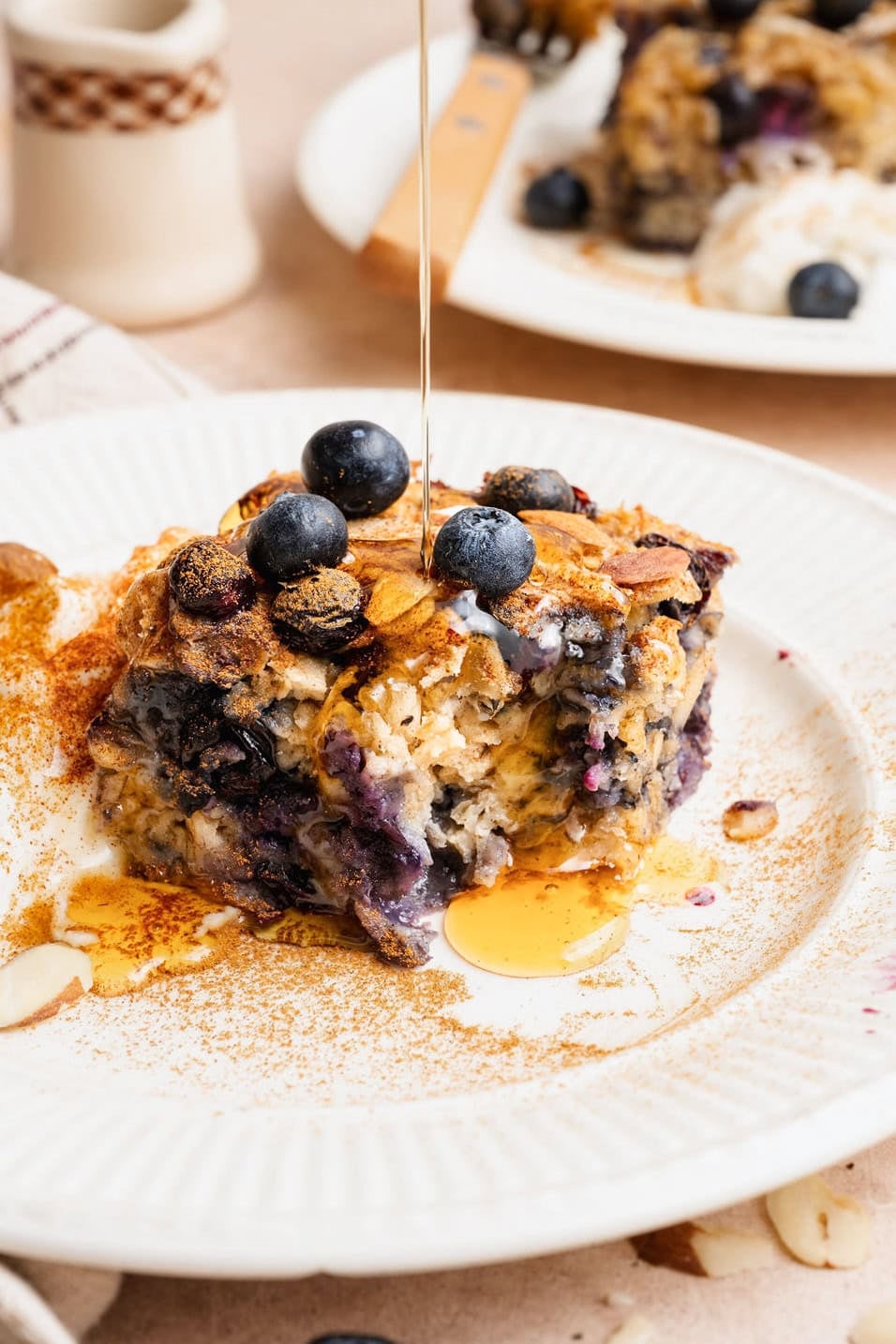 Close up view of a plate topped with a square of blueberry baked oatmeal drizzled with maple syrup and sprinkled with cinnamon