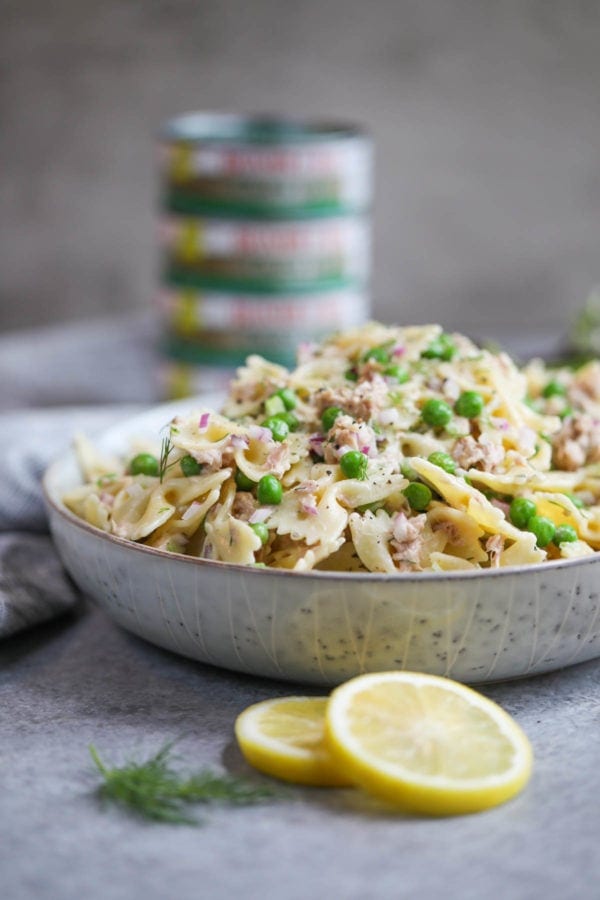 Close up side-view of a bowl of Lemon-Dill Tuna Pasta Salad with cans of tuna in the background. 