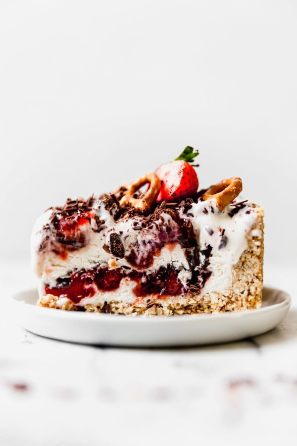 A sideview of a thick slice of Strawberry Pretzel Ice Cream Pie on a small white plate. 
