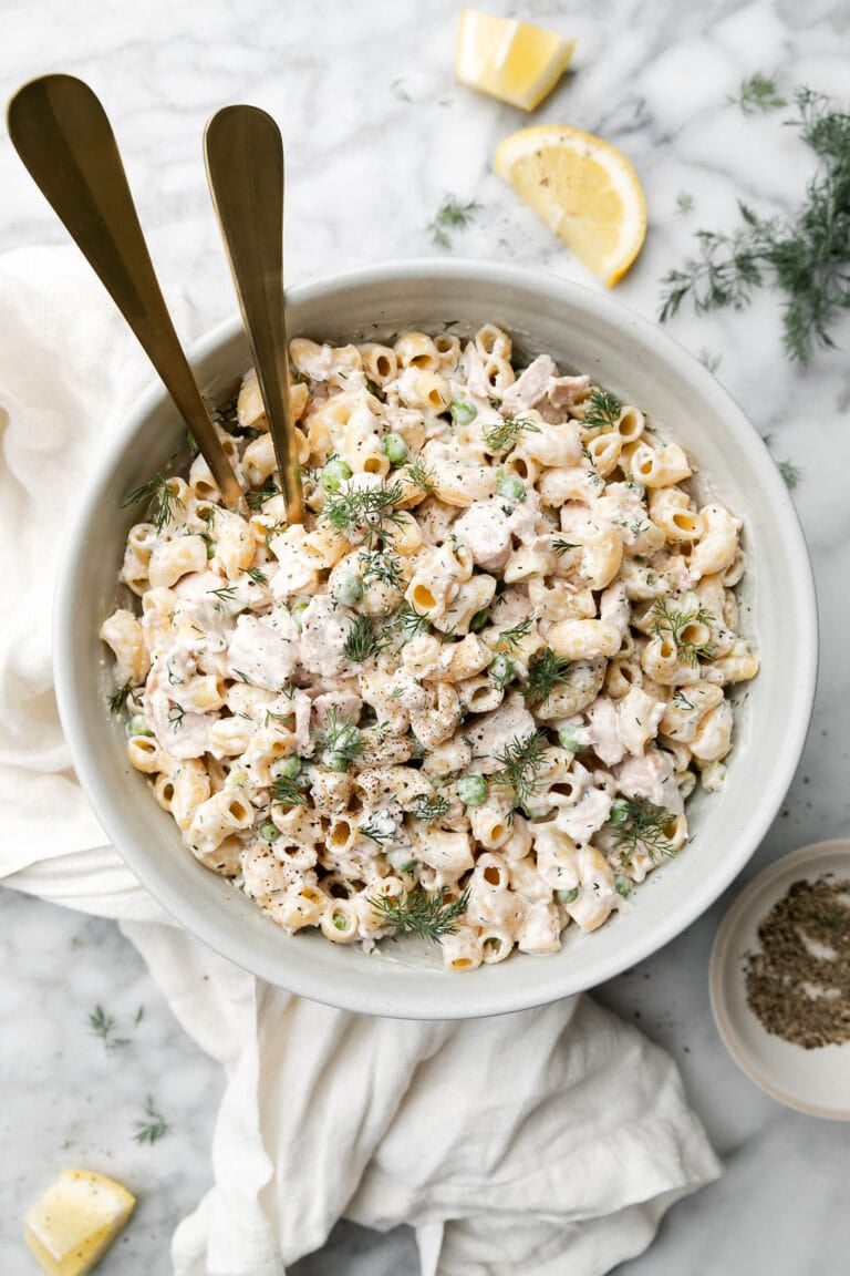 Overhead view of a white bowl of creamy tuna salad garnished with lemon wedges. 