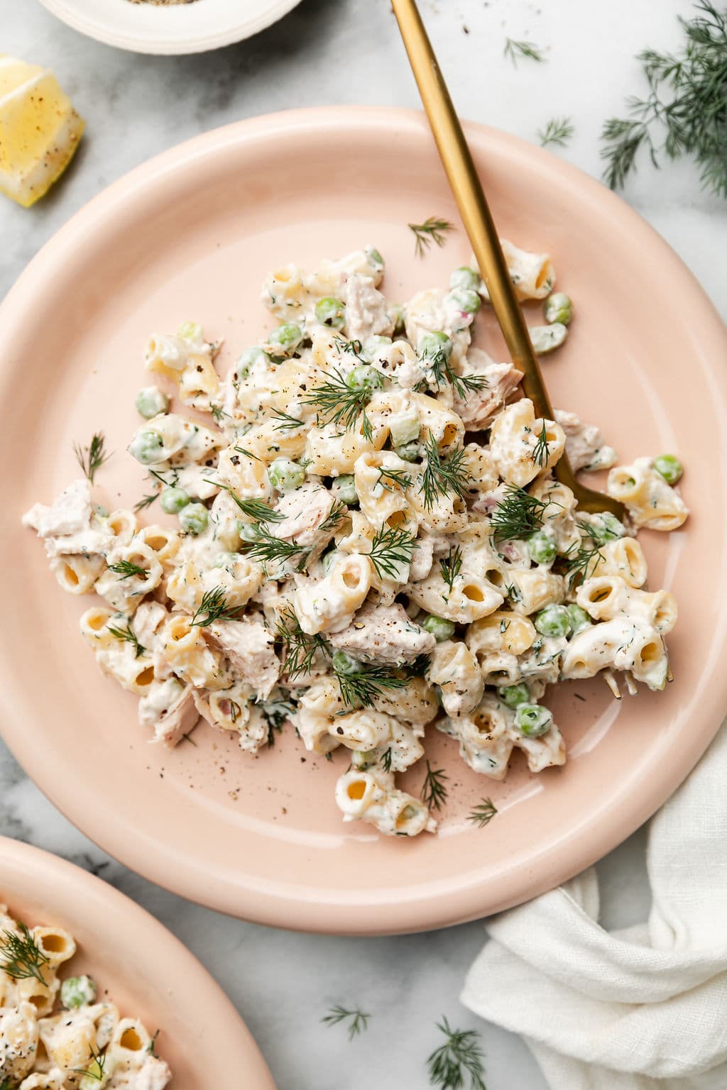 Serving of tuna pasta salad served on pink plate with fresh dill on top