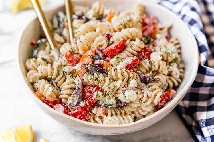 Greek veggie pasta salad with feta in serving bowl with gold cutlery