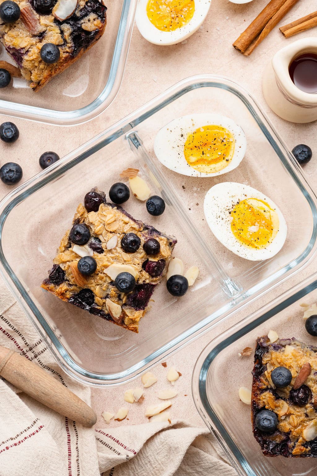 Overhead view of a 2-compartment glass meal prep container with a square of blueberry baked oatmeal on one side and a sliced hard-boiled egg on the other.