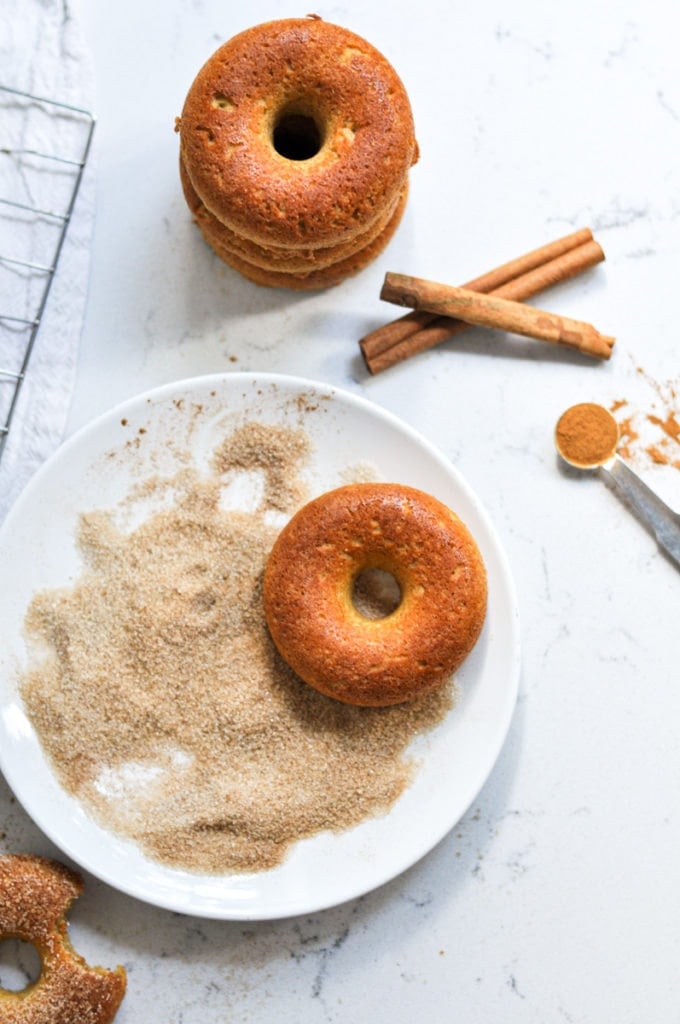 Baked Pumpkin Donut on a white plate showing the process of it being coated with cinnamon and sugar.