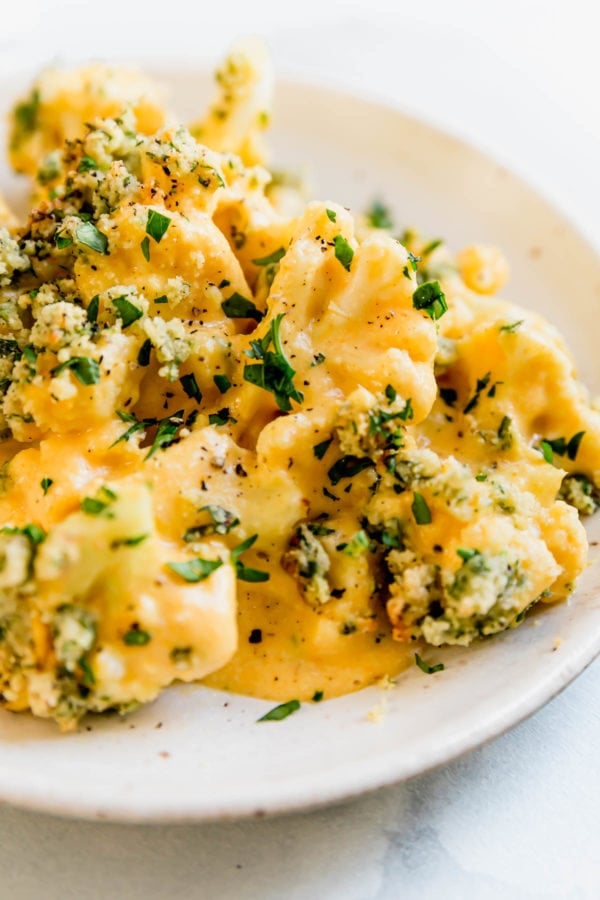 Close up view of creamy Paleo cauliflower mac and cheese with 'bread' topping and fresh herbs on a cream plate.
