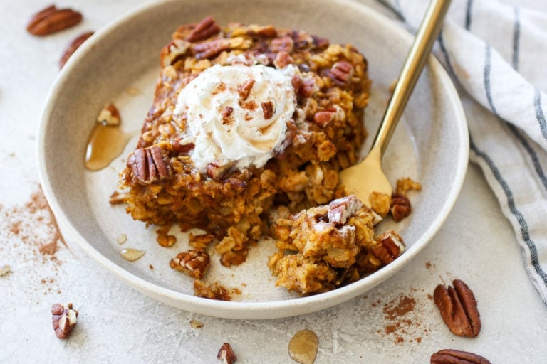 Overhead closeup view pumpkin baked oatmeal on plate, topped with whipped cream, cinnamon, and chopped pecans.